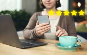 A woman using a smartphone with five stars on it and a cup of coffee.